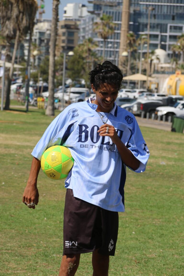 Player holding a TATU BOLA footvolley ball on the grass by the sea